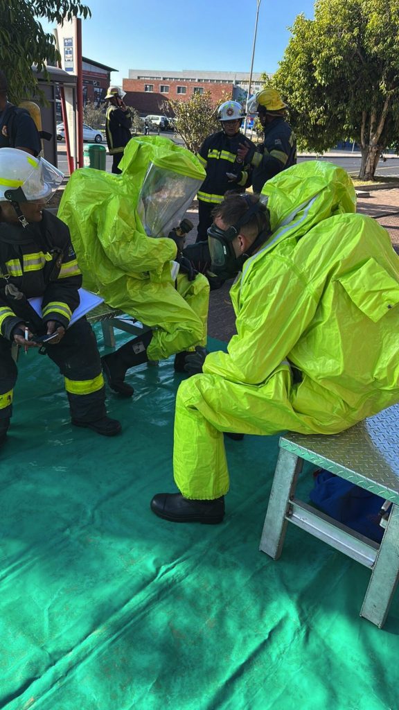 Hazmat technicians in fully encapsulated protective suits assess the scene during an active chemical incident