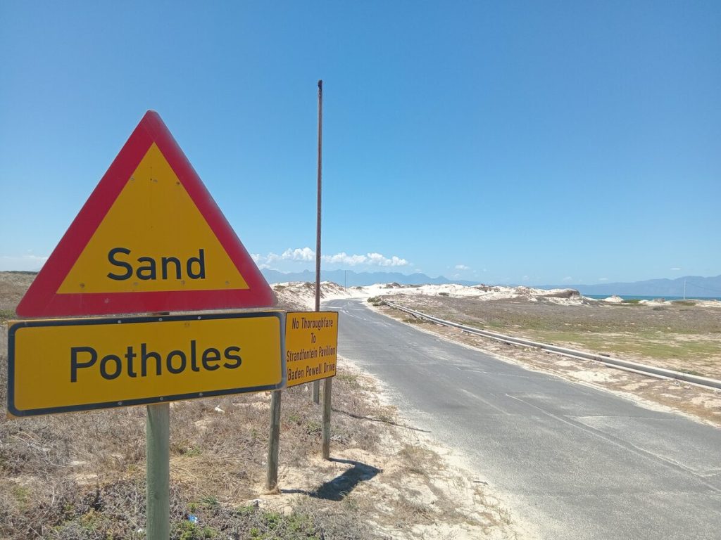 Signs warning of potholes and sand.
