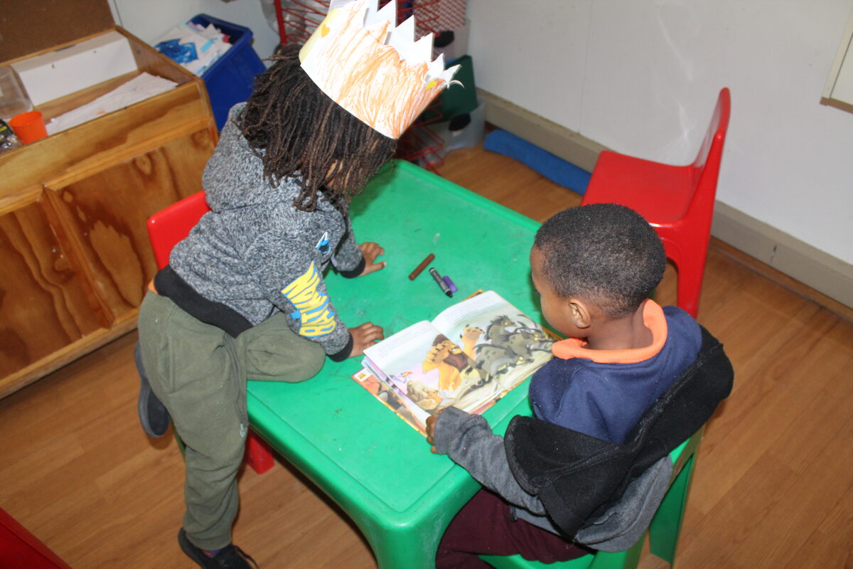 A little boy dons his paper crown while his friend reads at the trauma-informed holiday programme in Sewende Laan, Strandfontein.