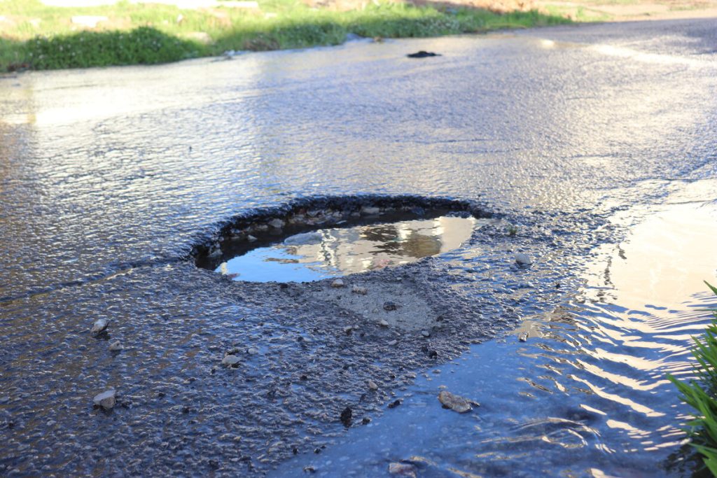 The unattended water leak has caused potholes in the street.