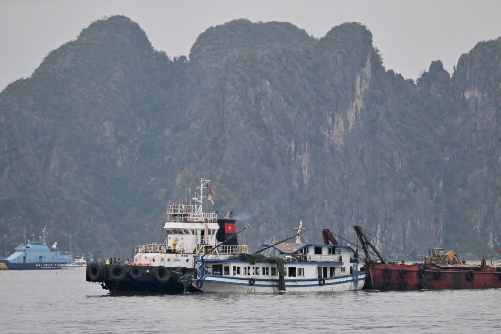 The tourist boat (C) that capsized is towed back to the port in Ha Long bay, Quang Ninh province on July 20, 2025. A tourist boat ferrying families around Vietnam's Ha Long Bay capsized in a storm on on July 19 afternoon, leaving at least 34 people dead, according to state media reports, as rescuers scrambled to locate the missing. (Photo by Nhac NGUYEN / AFP)