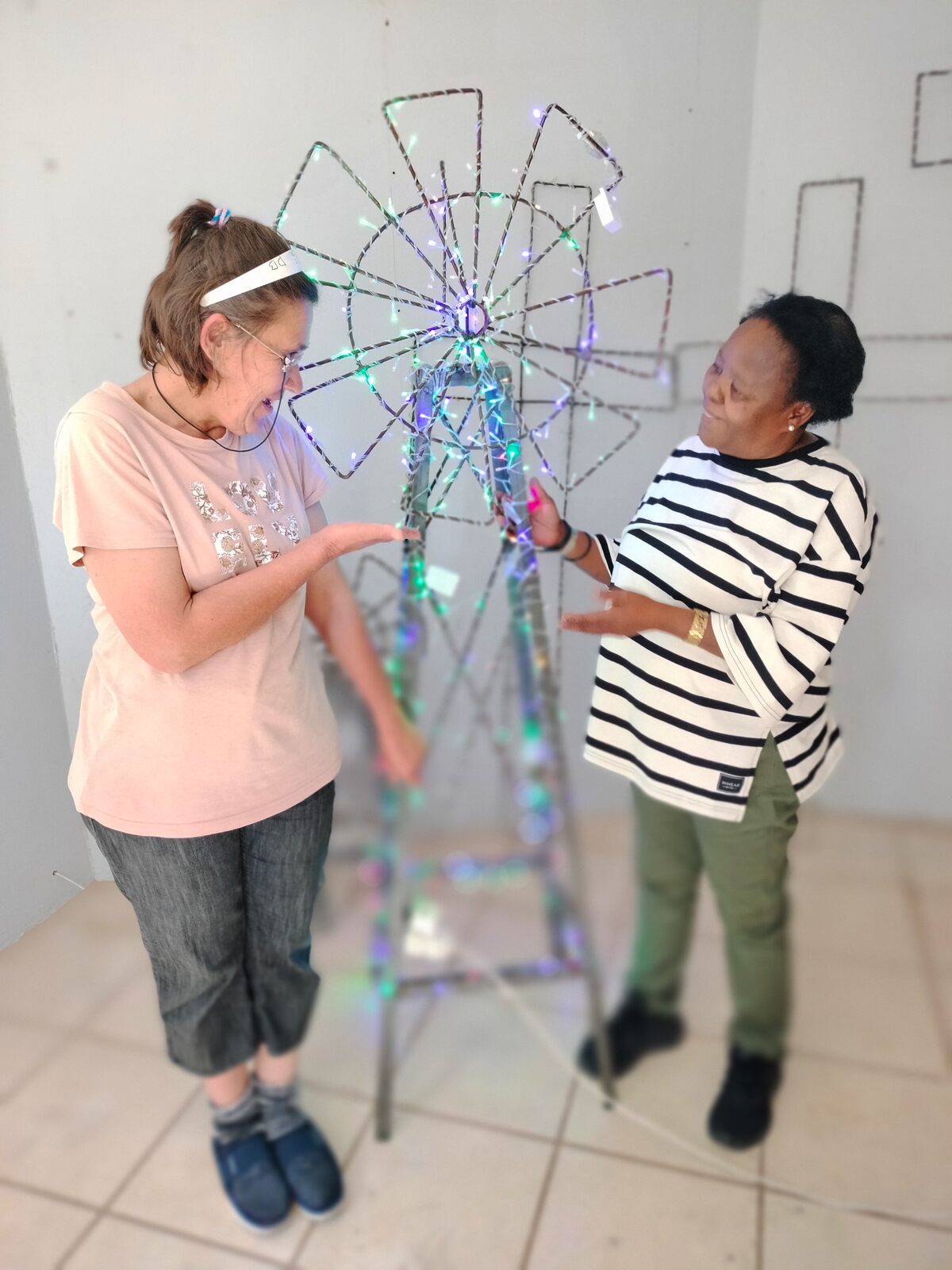 Donatella Bruwer, een van die werkers by die Vrystaat-nasorgsentrum, en Mirriam Mekgwe (toesighouer) by een van die windpompe wat met liggies versier is.