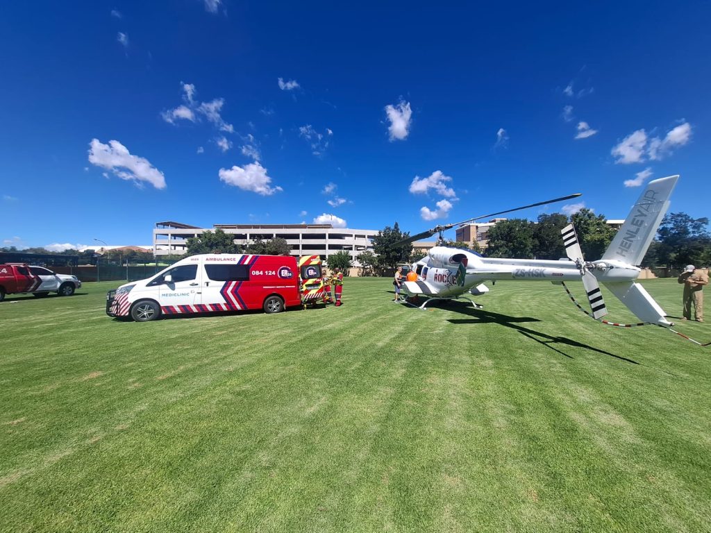 'n Pasiënt word uit een van die twee Rocket HEMS-ambulanse op die St Andrew's sportveld na die ER24-ambulans vervoer. Die Mediclinic Bloemfontein is in die agtergrond sigbaar. FOTO: Verskaf