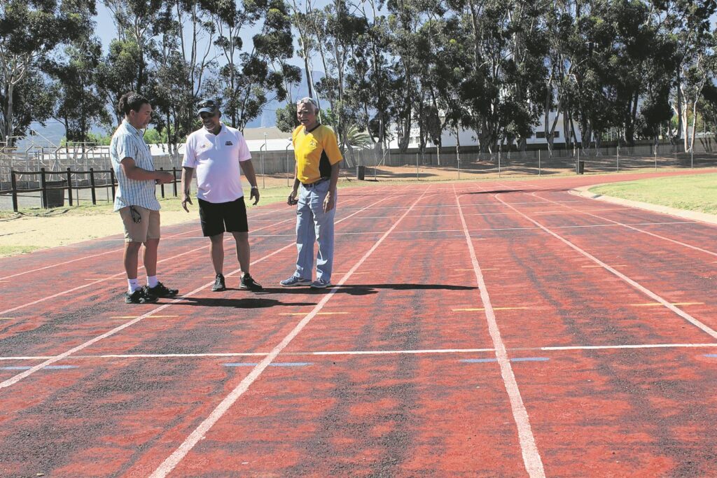Die foto wys drie mense op die Bolandpark-atletiekbaan wat erg verweer is.