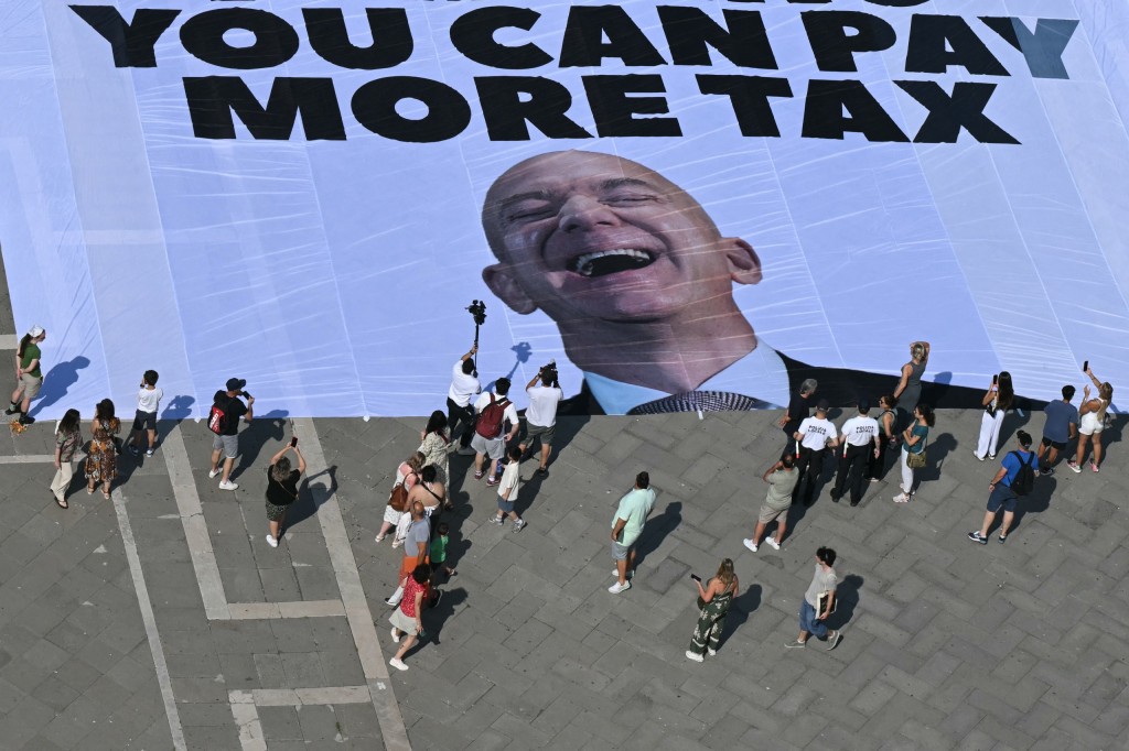 Activists of international environmental group Greenpeace deploy a giant banner displaying a picture of Jeff Bezos and reading "If you can rent Venice for your wedding you can pay more tax" at St Mark square in Venice yesterday. PHOTO: Stefano Rellandini / AFP