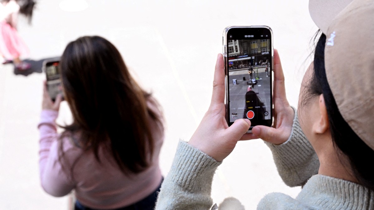 (FILES) A file photo taken on November 28, 2024 shows young people looking at their phones in Melbourne as Australia looks to ban children under 16 from social media. Tech companies including WhatsApp and Reddit as well as streaming giant Twitch and gaming firm Roblox could be among more than a dozen sites added to Australia's social media ban for under-16s, the country's regulator said on September 24, 2025. (Photo by William WEST / AFP)