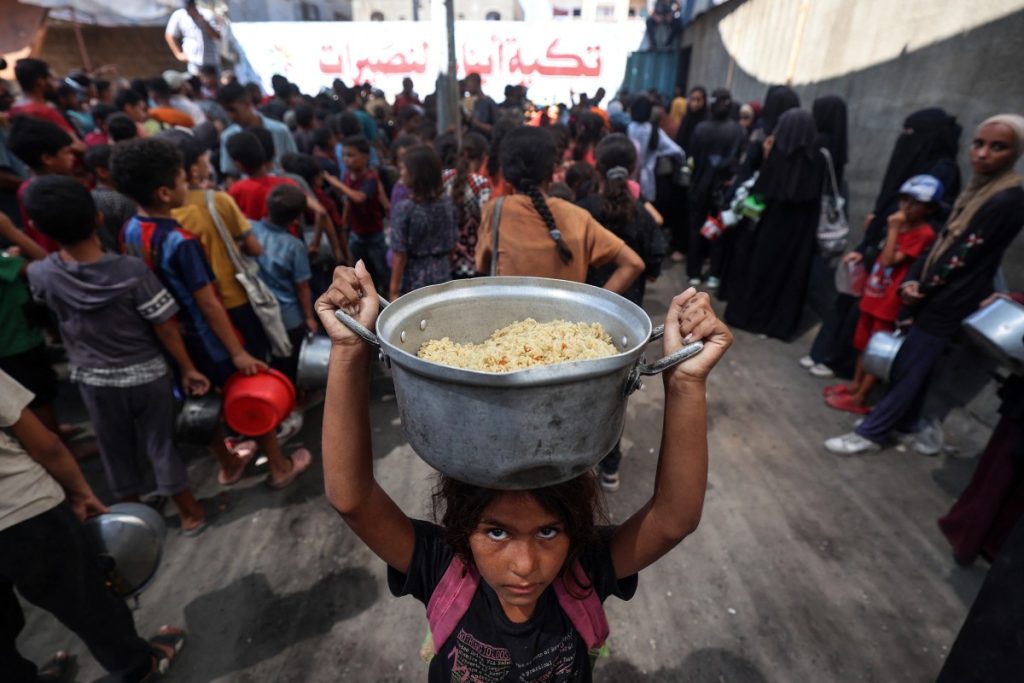 A Palestinian child walks away with a pot of rice obtained from a charity kitchen in the Nuseirat refugee camp in the central Gaza Strip, amid a UN-declared famine after nearly two years of war. (Photo by Eyad Baba / AFP)