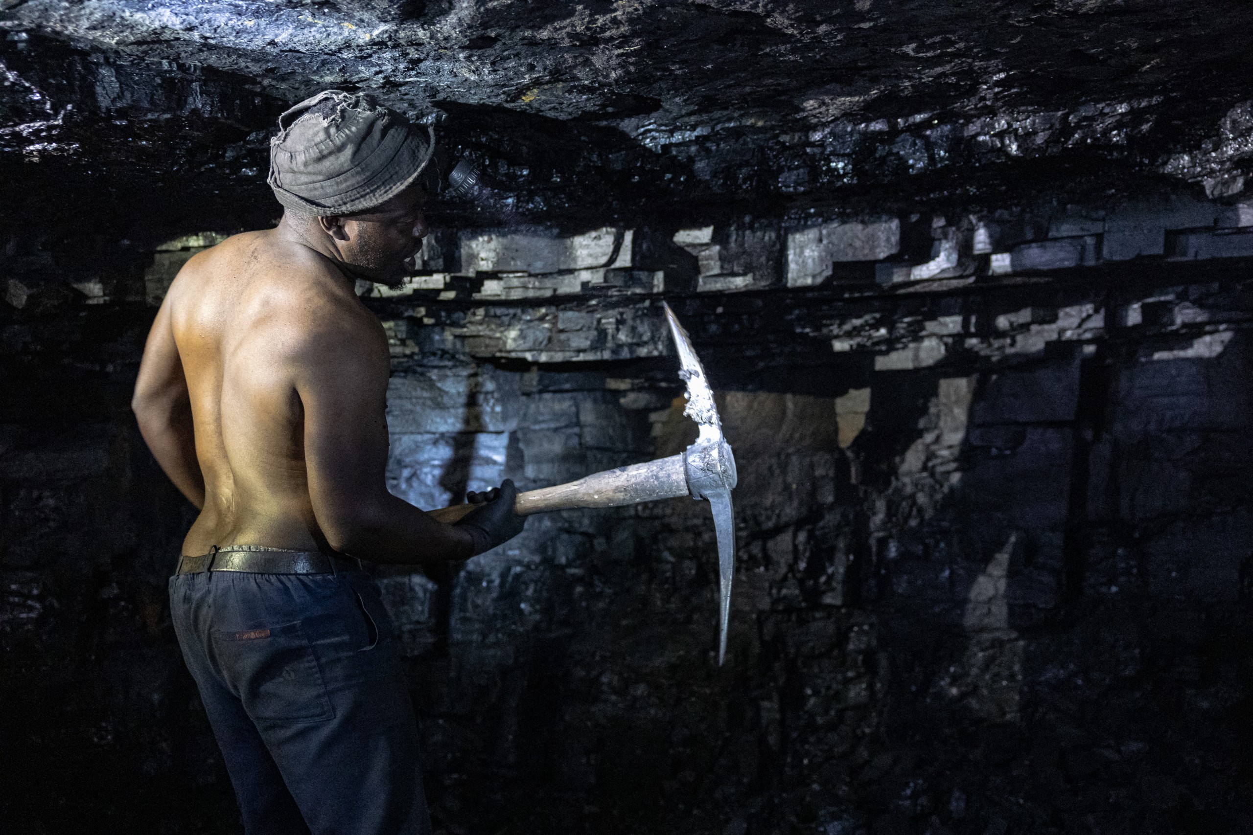 An artisanal miner emerges from an abandoned coal shaft near Ermelo, Mpumalanga Province, where dozens of unemployed men risk dangerous conditions daily to extract coal for local communities. South Africa's transition to green energy has left many informal miners uncertain about their economic future."