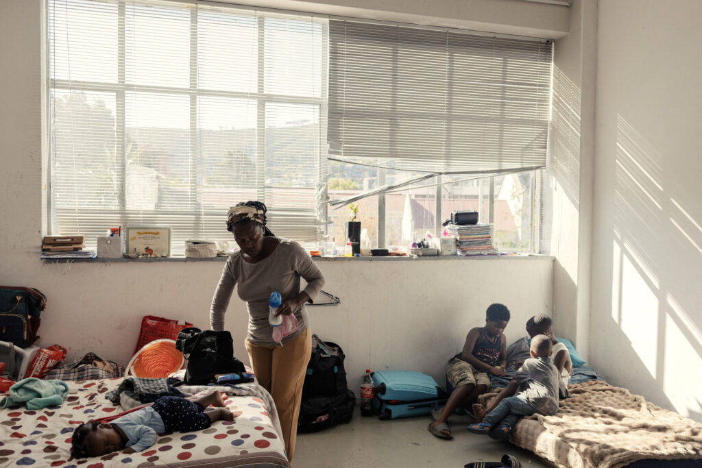 A woman tends to her children in one of the spaces transformed in a living quarte inside an occupied building in downtown Cape Town on December 18, 2025. Nestled between spectacular mountains and the Atlantic Ocean, Cape Town has emerged as a growing tourism destination, topping in 2025 the Telegraph and Time Out magazine's rankings of best cities in the world. Activists say the drive to profit from tourism accommodation is pricing locals out of coveted neighbourhoods, including areas near District Six -- a site long associated with the apartheid-era removals that displaced non-white communities to remote, underdeveloped townships. (Photo by GIANLUIGI GUERCIA / AFP)