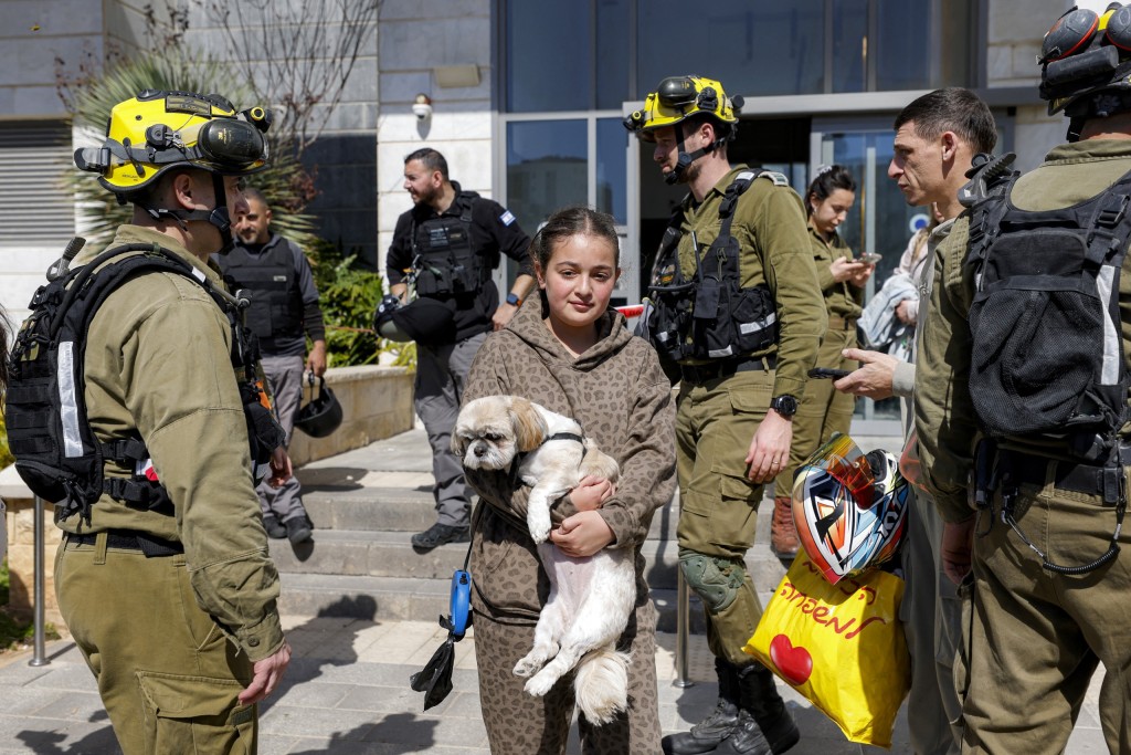 A girl walks carrying a dog as residents of a building hit by a projectile are evacuated.