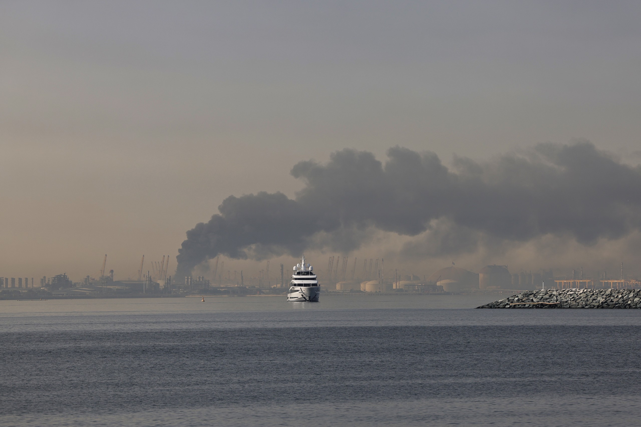 A yacht sails past a plume of smoke rising from the port of Jebel Ali following a reported Iranian strike in Dubai on Sunday 1 March. Ships have been told to stay away from the Gulf due to ongoing military activity. Photo by Fadel Senna / AFP
