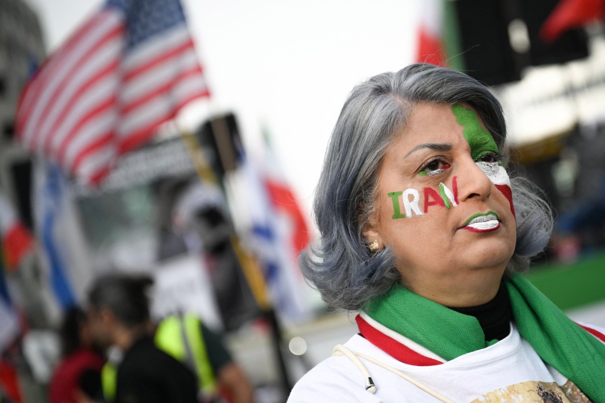 A supporter of Iran's last crown prince, now key opposition figure, Reza Pahlavi, looks on wearing makeup reading "Iran" and bearing Iran's national colours as she takes part in a march for Iran in Paris on 7 March, amid the ongoing war in the Middle East.