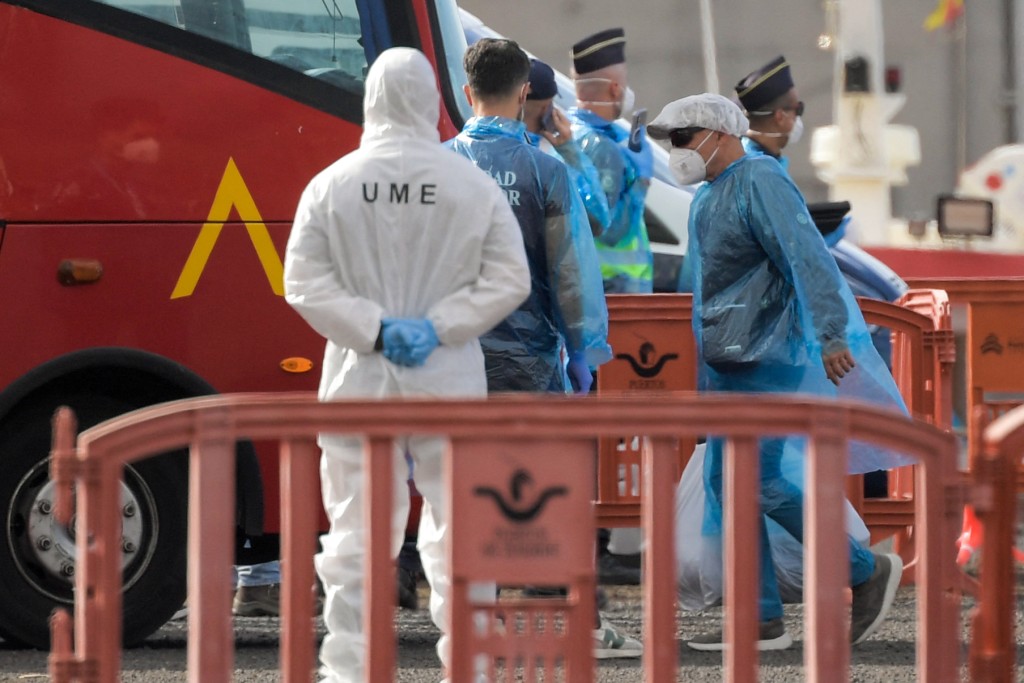 A passenger wearing a blue protective suit boards a military bus after being evacuated from the ship.