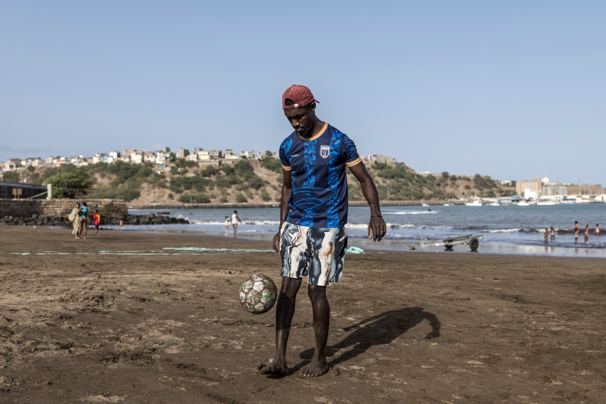 A man wearing a Cape Verde football jersey juggles a football at Gamboa Beach