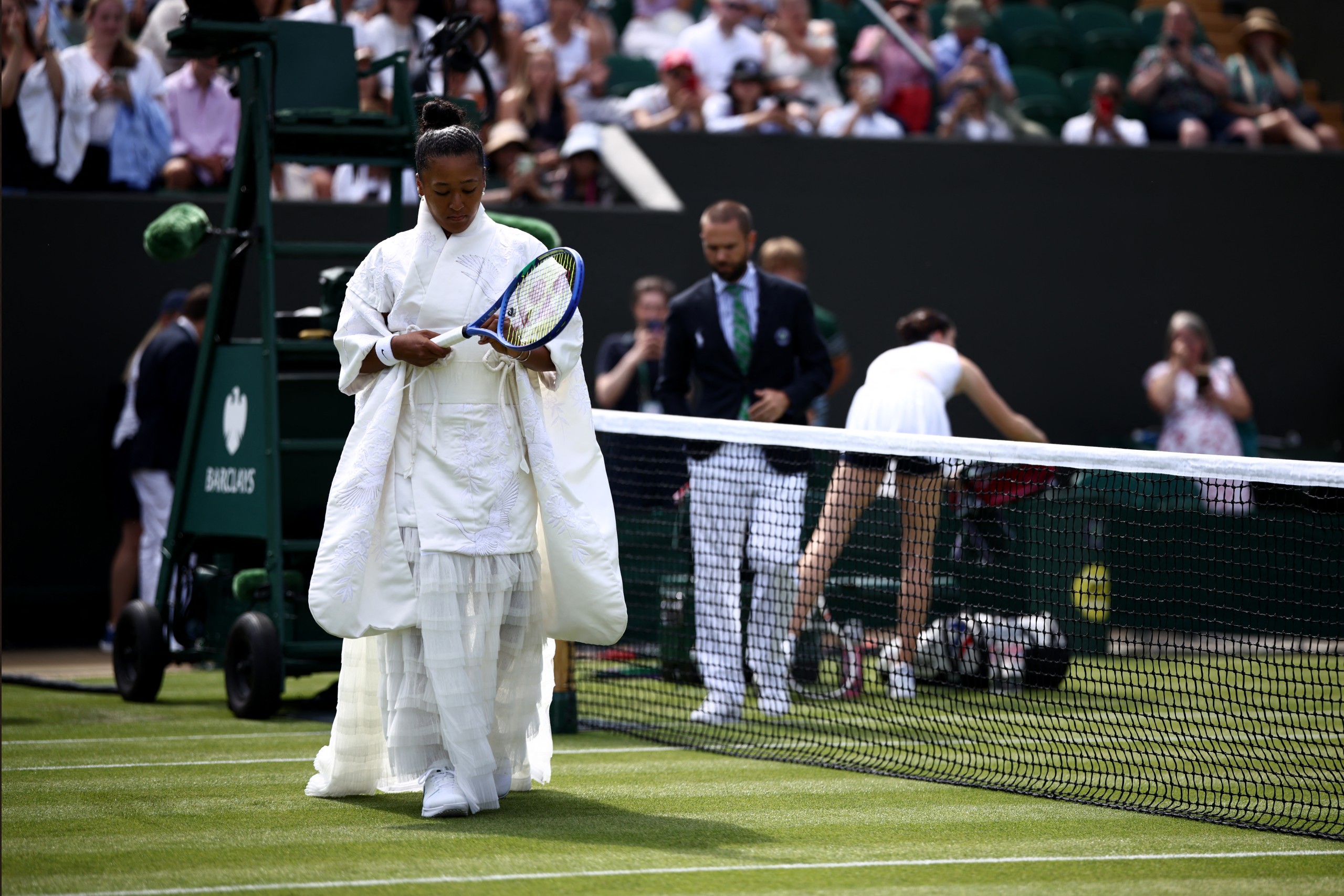 Naomi Osaka arrives on court in a white kimono-style dress