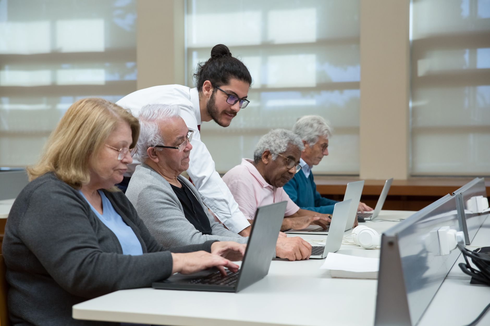 a man teach a group of elderly to use a laptop
