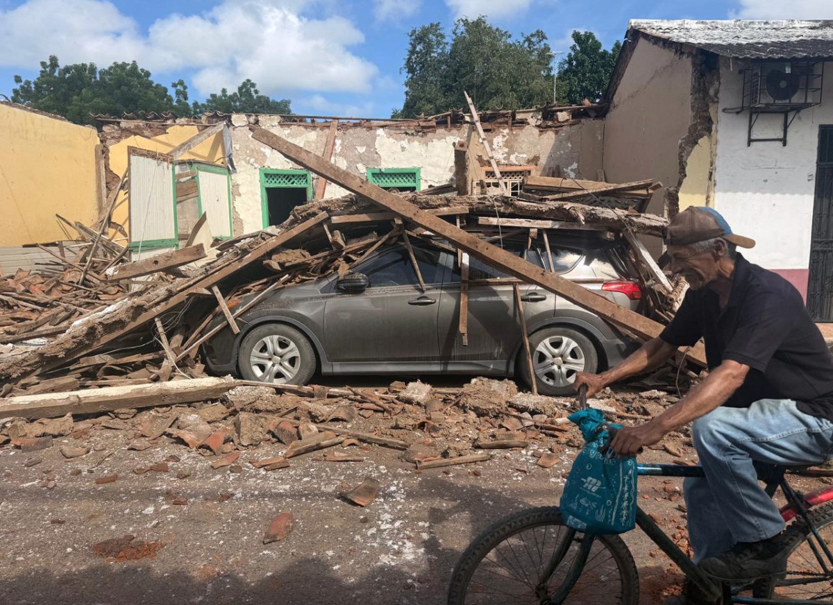 A man rides a bicycle past a collapsed house and a car buried under debris in the town of Chitre, about 250 km southwest of Panama City.