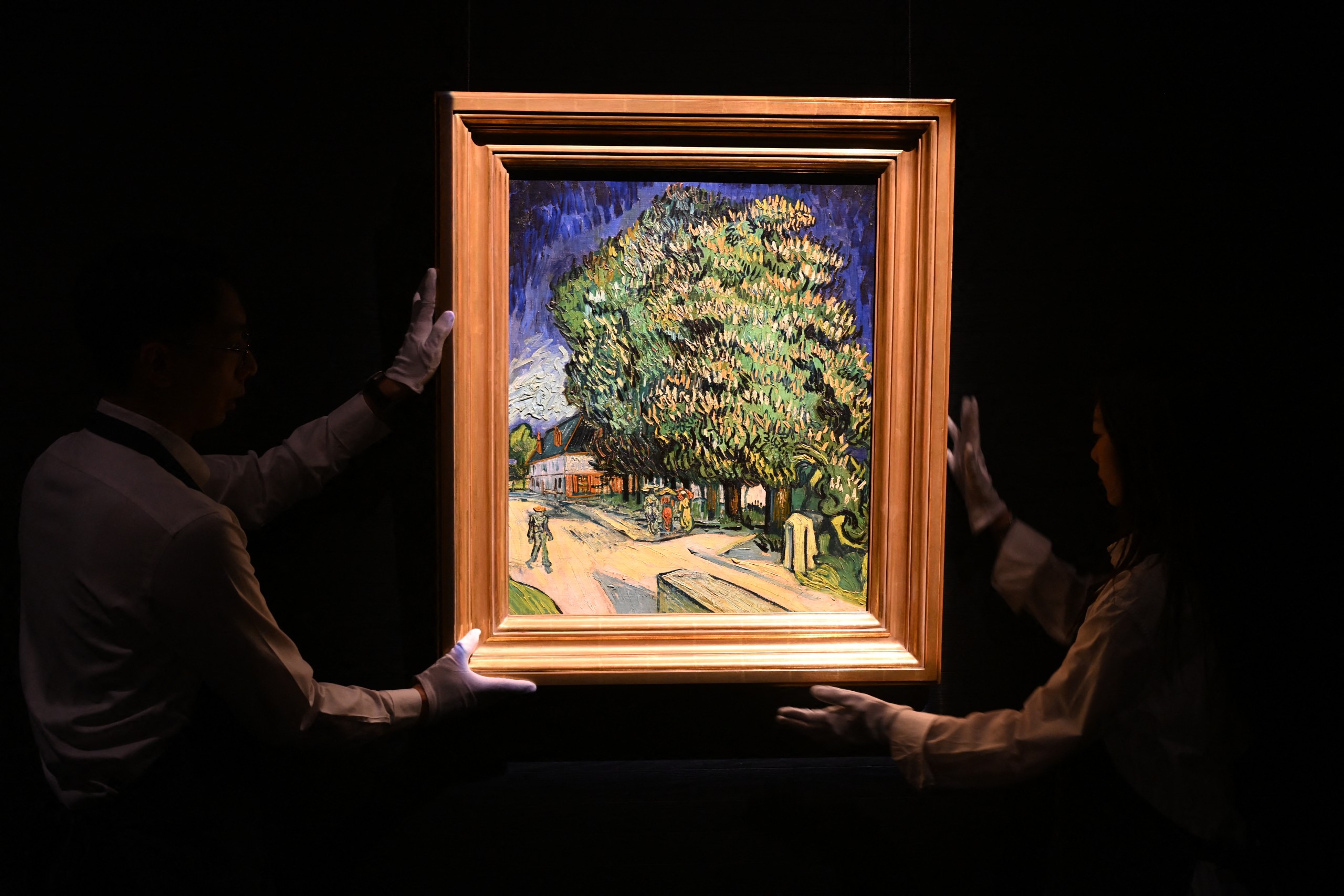 Sotheby's staff handle the "Châtaigniers en fleurs" (Chestnut Trees in Blossom) painting by Vincent van Gogh at an auction preview in Hong Kong on October 13, 2026. Painted during the final months of the artists life in Auvers-sur-Oise, it will be auctioned in New York in November 2026 with an estimated price in the region of USD 180 million. (Photo by Peter PARKS / AFP) /