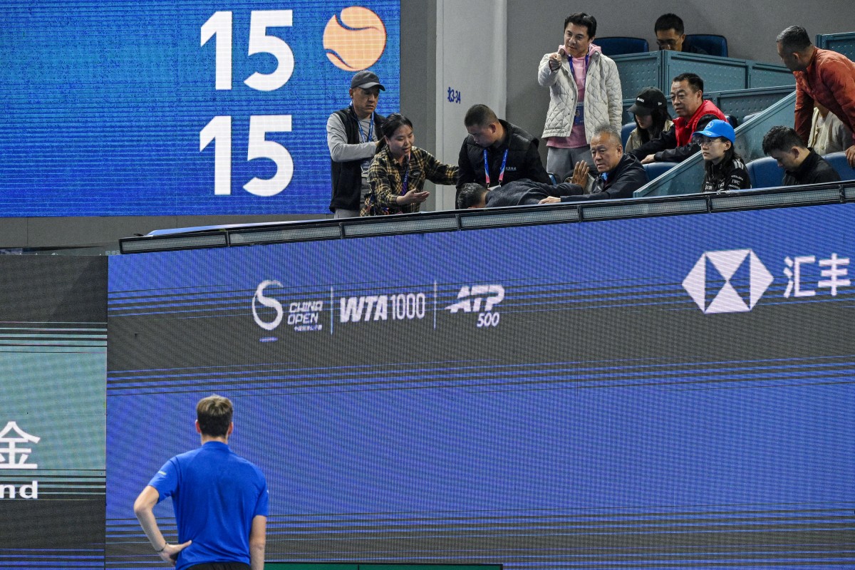 A spectator points at Russia's Daniil Medvedev (bottom) as another spectator (4L) is assisted after he was injured by a ball Medvedev hit into the stands