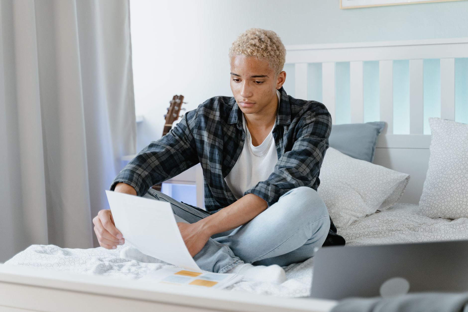 a student sitting on his bed while holding a paper